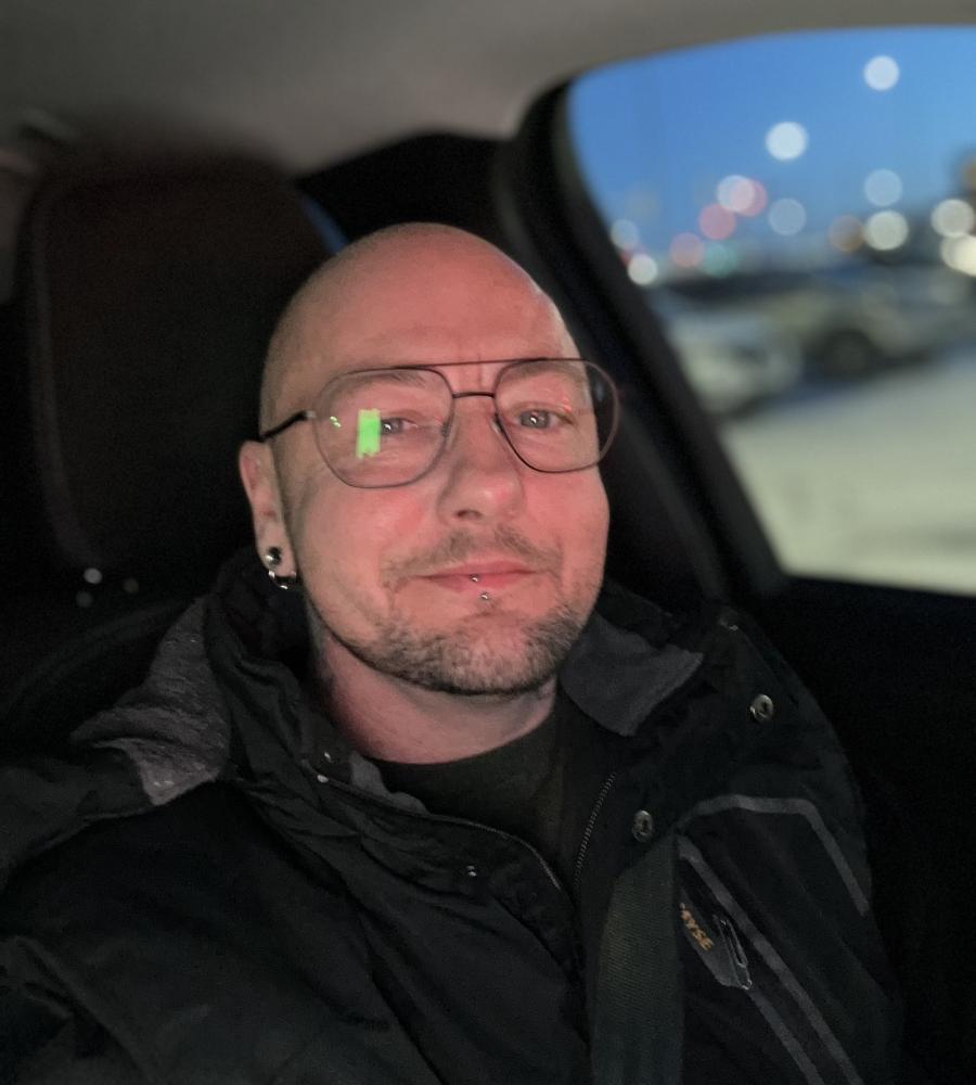 Ceder has a black jacket on and is wearing glasses 