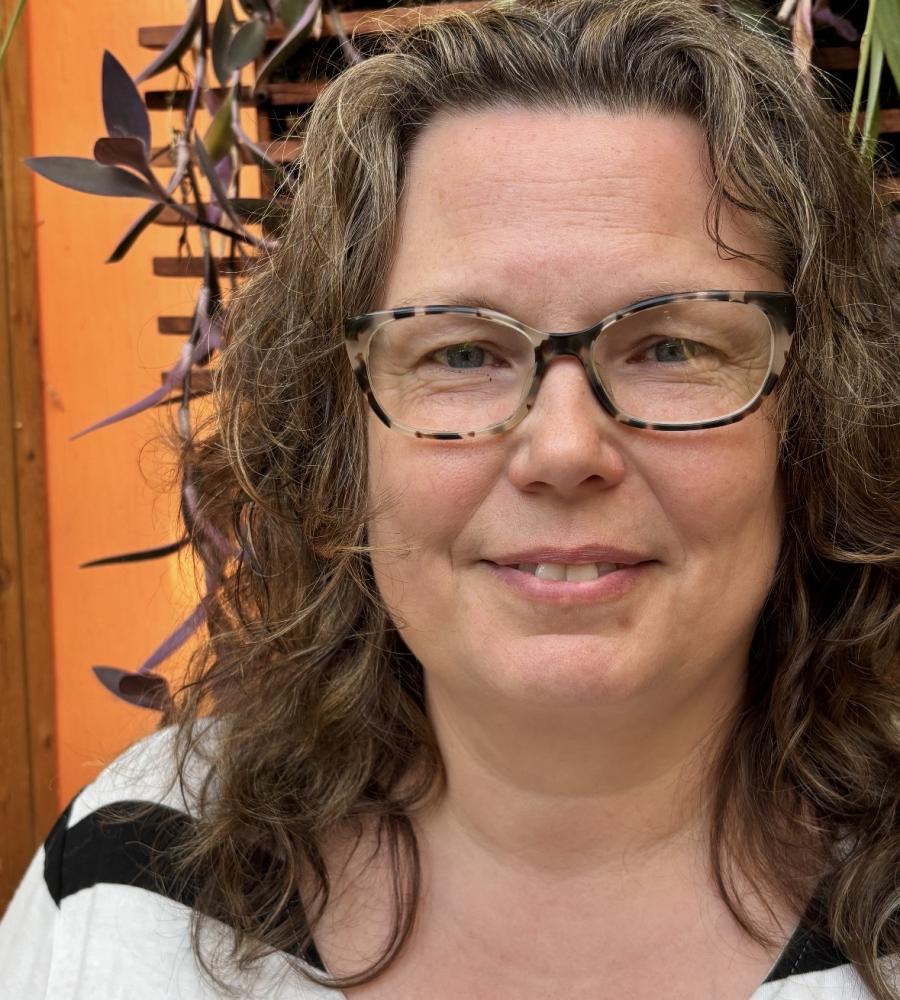 Rhoda has shoulder length hair and wearing glasses with a slight smile 